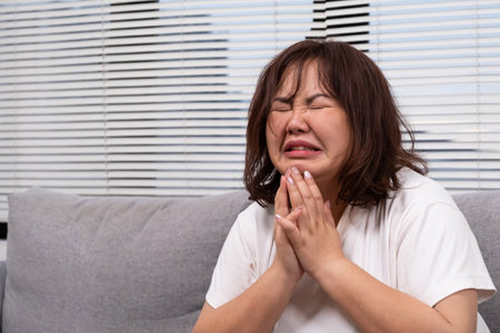 Close up shot of Young Asian girl crying while sitting on sofa inside of living of the house. Sad and stress emotion expression of chubby overweight Asian women with copy space for text.の写真素材