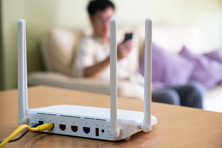 Selective focus at router. Internet router on working table with blurred man using smart phone at the background. Fast and high speed internet connection from fiber line with LAN cable connection.の写真素材