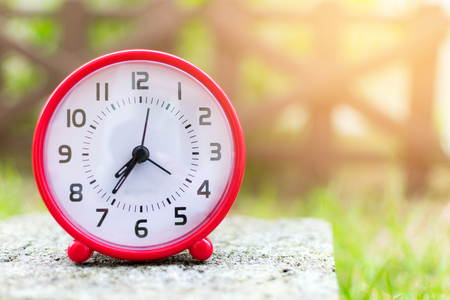 The red clock holding on the floor in the garden background.