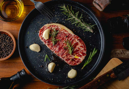 Raw fresh beef steak with olive oil, Colorful pepper, garlic and the rosemary leaf fresh on in the black tray on the wooden table, Top view.の写真素材