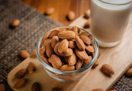 Almond milk in the glass with almond in the glass bowl on the wooden table.の写真素材