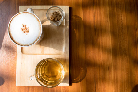 cup of cappuccino with sugar and cup of tea on wooden tableの写真素材