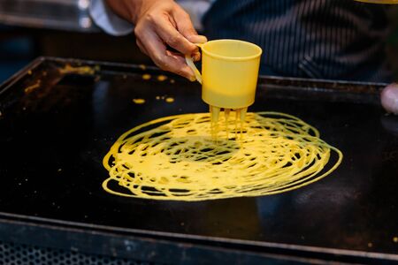 a cook makes a circular motion to create lace pancake or roti jala as it is commonly known as in...