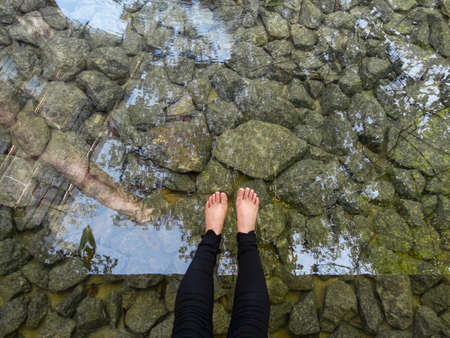 Top down view of a woman's leg hanging over a body of water with rocks