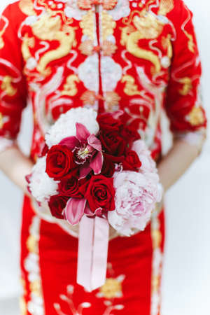 Close up of a bride holding a hand bouquet of flowers in a Chinese wedding ceremonyの写真素材