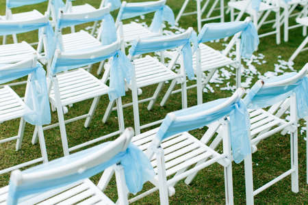 View of white chairs with blue ribbons during a garden wedding ceremonyの写真素材