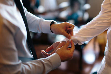 View of a man helping another man to wear his cufflink on his shirt