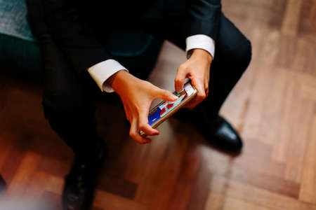 Close up of a man in tuxedo playing an electronic game on his cell phoneの写真素材