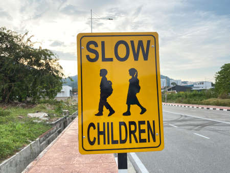 Close up view of a yellow road sign with "SLOW CHILDREN" which reminds vehicles to reduce speed due to school childrenの写真素材