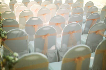 View of chairs in white covers with pink ribbons during a beach weddingの写真素材
