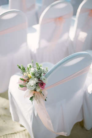 View of chairs in white covers with pink ribbons during a beach weddingの写真素材