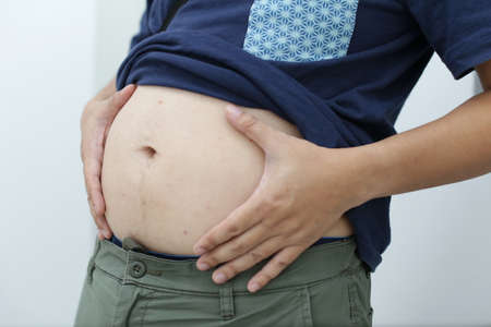 View of an adult male holding his big belly with his shirt upの写真素材