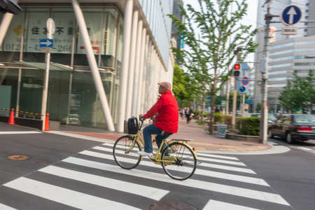 A senior citizen cycling along the streets of Osaka Japan.のeditorial素材