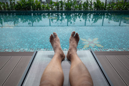 An adult male sitting on a deck chair by the side of a swimming pool on a hot dayの写真素材
