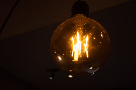 Close up of a lightbulb hanging from a ceiling inside a dark roomの写真素材