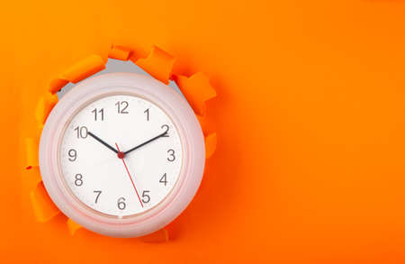 clock showing up from torn orange paper. Copy spaceの写真素材