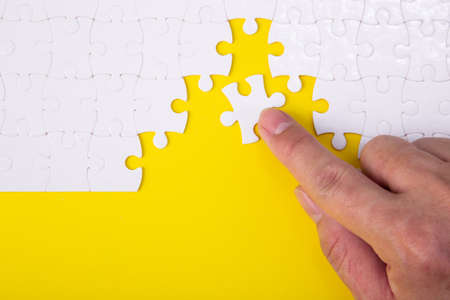 Hand putting the a piece of white jigsaw puzzle on color background and place for your content