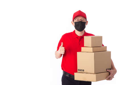 young Asian delivery man in red uniform with  face mask, carrry cardboard box in hands isolated on white background. Delivery conceptの写真素材