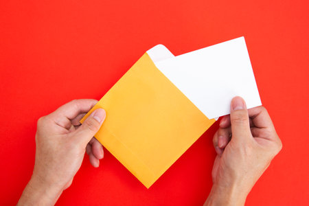 Hand holding a blank white card in color envelopeの写真素材