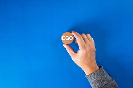 Businessman hand holding a round wooden block  with the word ego written on it.の写真素材