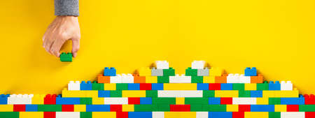 hand building up a wall by stacking up colorful plastic block