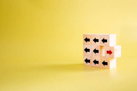 Wooden block with red arrow facing the opposite direction black arrows, think different and standing out from the crowd conceptの写真素材