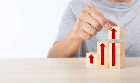 Hand arranging wood block stacking as step stair with arrow up. Ladder career path concept for...