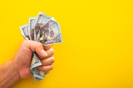 Male hand squeezing tightly some banknote on yellow background