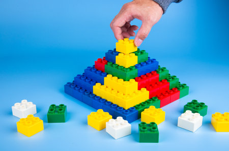 hand building up a wall by stacking up plastic block on blue backgroundの写真素材