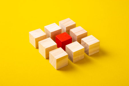 Red wooden block standing out from the group wooden blocks on yellow background.の写真素材