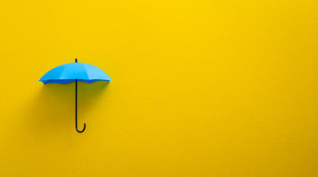 Blue toy umbrella on yellow background. Insurance coverage concept.の写真素材
