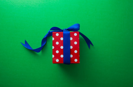 Red gift box with blue ribbon on green backgroundの写真素材