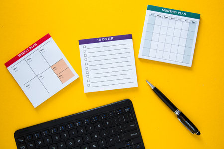 Manager organizing week using calendar, monthly planner and to do list on yellow desk