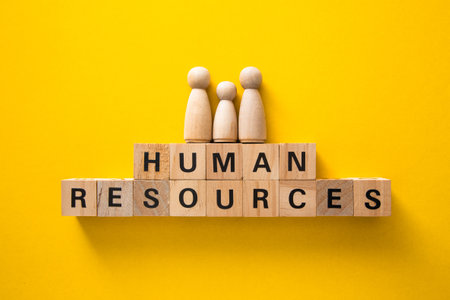 Wooden family figurines standing on top of human resources message spelled on wooden blocks over bright yellow backgroundの写真素材