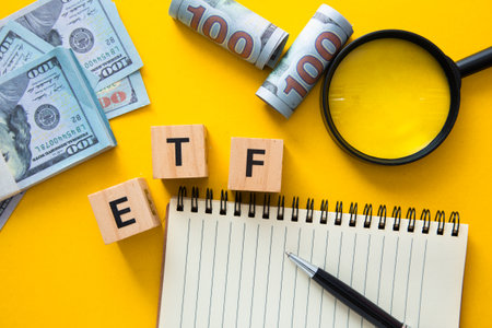Etf word on wooden cubes with magnifying glass, pen and notepad on yellow table, top view
