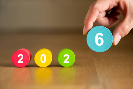 Hand adding the last number to complete the year 2026 made of colorful wooden pieces on a wooden...