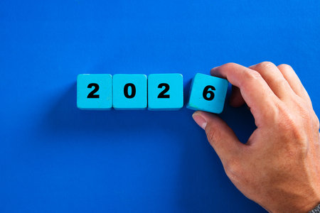 Hand arranging blue cubes to represent the year 2026 on a blue backgroundの写真素材