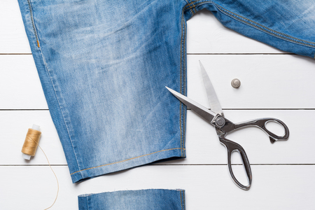 Cutting jeans with a tailor scissors to make  shorts on white wooden tableの写真素材