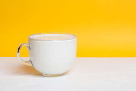 Glass cup full of milk on white wooden table. Yellow backgroundの写真素材