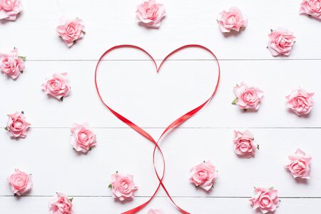 Red ribbon heart symbol with pink roses on white wooden backgroundの写真素材