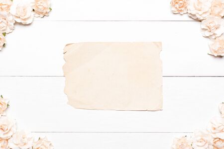 Old paper sheet with empty copyspace and roses on white wooden backgroundの写真素材