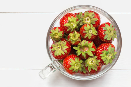 Glass cup full of strawberries on white wooden table flat viewの写真素材