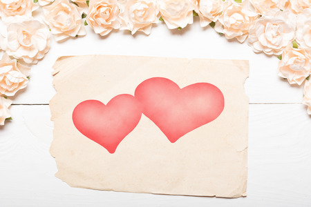 Paper sheet with two hearts and white roses on painted wooden tableの写真素材