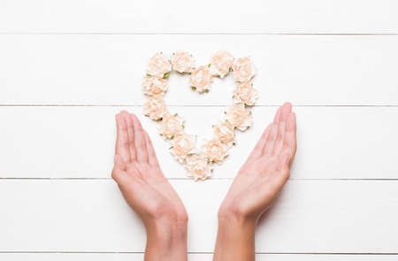 Young hands holding heart made of white rosesの写真素材