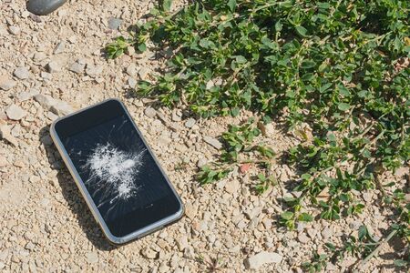 Broken mobile phone on sand concept background