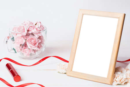 Photo frame on white wooden table. Ribbons and roses background