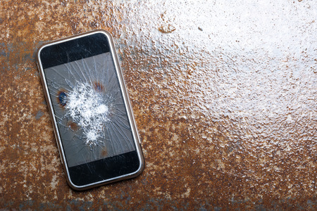 Broken Phone with cracked screen on wet metal backgroundの写真素材