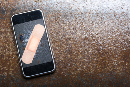 Smartphone with cracked screen fixed with sticking plaster. Wet metalの写真素材