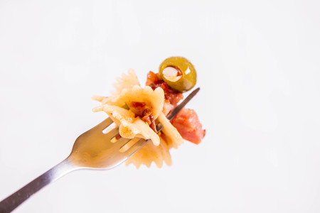 Farfalle pasta with sun dried tomatoes, ham and olives on a white backgroundの写真素材