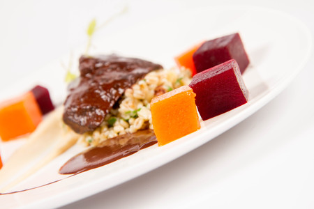 Beef cheeks with vegetables, roasted parsley root mousse, pearl barley, dark chocolate and demi glace sauce on a white backgroundの写真素材